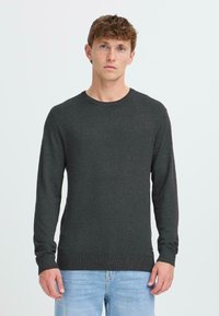 Suéter de punto gris oscuro con mangas largas, cuello redondo y puños acanalados. Combinado con jeans de mezclilla azul claro.