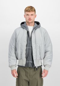 Grå polstret jakke med en glatt tekstur, med et quiltet design og ribbede mansjetter, lagd over en grå hettejakke med glidelås.