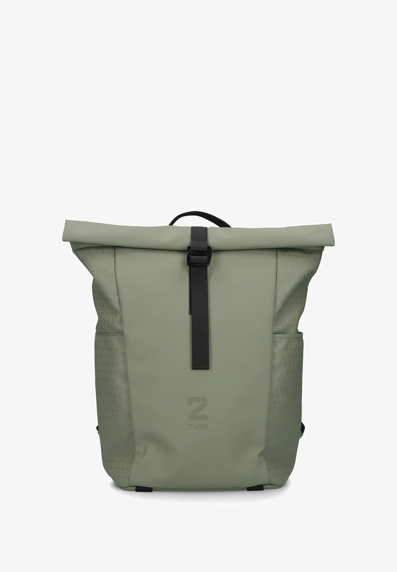 Sac à dos à rabat en vert olive, avec côtés texturés, sangle noire et bouclerie, et accents à motif triangulaire sur les poches.