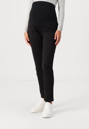 Zwarte zwangerschapsbroek met een hoge, rekbare tailleband en taps toelopende benen. Gemaakt van zacht stof, gecombineerd met witte sneakers.