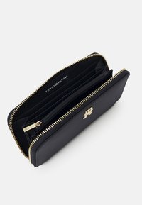 Črn usnjen denarnica s pozlačenimi dodatki in zadrgo, večimi režami za kartice ter centralnim predalom na zadrgo. Vidna jeloga "TOMMY HILFIGER".