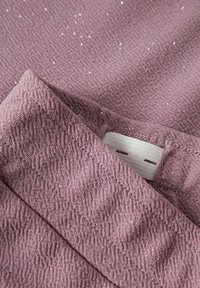 Tissu texturé violet avec de subtiles paillettes, plié pour mettre en valeur les coutures et une étiquette blanche. La surface présente un tissage à motifs.