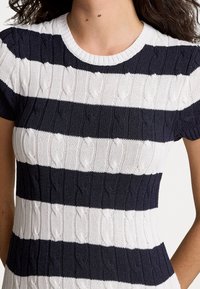 Stickad klänning med horisontella marinblå och vita ränder, kabelmönstertextur, rund hals och korta ärmar, tillverkad av ett elastiskt material.