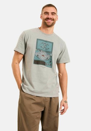 Jasnoszara koszulka z grafiką vintage gramofonu i tekstem. Krótkie rękawy, okrągły dekolt, luźny krój. Połączona z beżowymi spodniami.