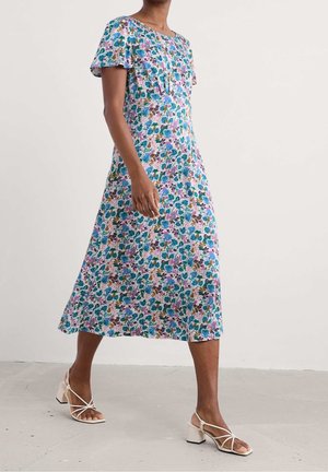 Robe midi fleurie avec manches courtes à volants, motifs floraux multicolores sur un fond clair, et coupe décontractée. Portée avec des talons à brides.