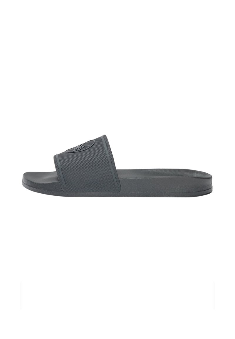Grå slide-sandal med en texturerad rem och en platt sula, tillverkad av flexibelt material med en cirkulär logotyp som accent på remmen.