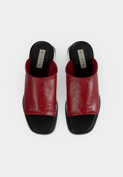 Ζευγάρι κόκκινα δερμάτινα σανδάλια slide με μαύρες σόλες και τετράγωνη μύτη, θέα από πάνω σε λευκό φόντο.