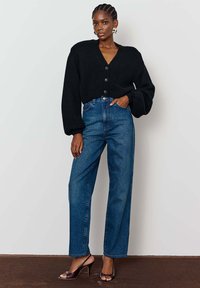 Juoda megzta trumpa kartu su V formos iškirpte, su apvaliais mygtukais. Derinama su aukštu liemeniu mėlynomis džinsinėmis kelnėmis ir atvirais bateliais.