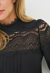 Czarna bluzka z misternymi koronkowymi detalami na dekolcie i ramionach, z plisowanym materiałem i gładką fakturą.