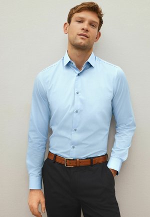 Light blue long-sleeve button-up shirt with a structured collar and fabric texture, paired with dark trousers and a brown belt.