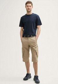 Marineblå t-shirt med korte ærmer, letvægtsbrune cargo shorts med flere lommer og sorte sneakers; afslappet pasform med et bælte.