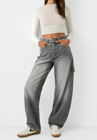 Spodnie dżinsowe o szerokich nogawkach w bladych szarościach z wysokim stanem, z kieszeniami z przodu, szlufkami na pasek i luźnym krojem. Połączone z dopasowaną białą bluzką.