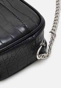 Czarna torebka na ramię z eko skóry z tłoczeniem imitującym krokodyla, z srebrnym łańcuszkowym paskiem, prostokątnego kształtu, błyszcząca o subtelnych szczegółach przeszyć.
