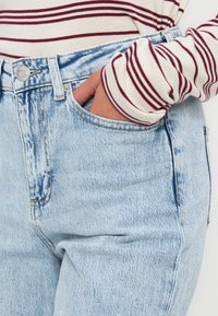 Ljusblå hög midja jeans har en klassisk femfickdesign, blekt utseende och metallknappdetaljer, i kombination med en randig ärm.