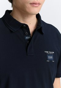 Navyblauwe polo met een klassieke kraag, een placket met drie knopen en een patch met branding op de linkerborst. Van katoen met een gestructureerde afwerking.