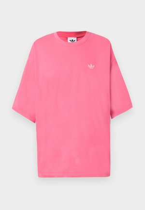 Svetlo roza Adidas majica s kratkimi rokavi in majhnim belim logotipom trikrake deteljice na levi prsni strani, prikazana na enostavni podlagi.