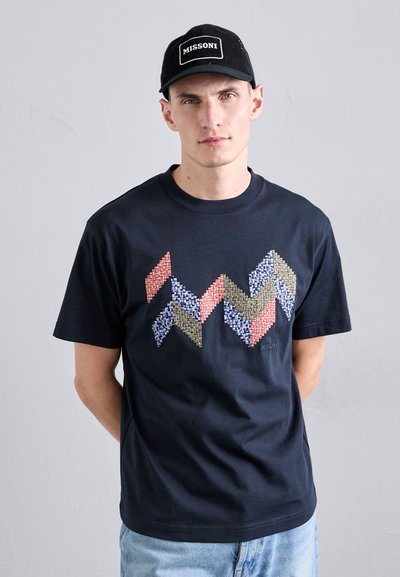 Jūrų karininkų stiliaus medvilninis marškinėliai su geometrine daugiaspalve austo rašto chevron formomis. Derinama su juodu kepurėliu su "MISSONI" logotipu.