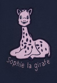 Giraffa rosa ricamata con macchie nere, sorridente, di fronte al testo "Sophie la girafe," su uno sfondo di tessuto blu scuro.