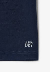 Granatowa koszulka sportowa z oddychającej tkaniny; posiada białe logo "ULTRA DRY" na dolnym brzegu; minimalistyczny design, bez dodatkowych akcentów.