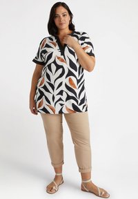 Kortärmad tunika med ett mönster i svart, vitt och rostfärgad blad; har en V-ringning och är kombinerad med beiga byxor med uppvikt ärm.