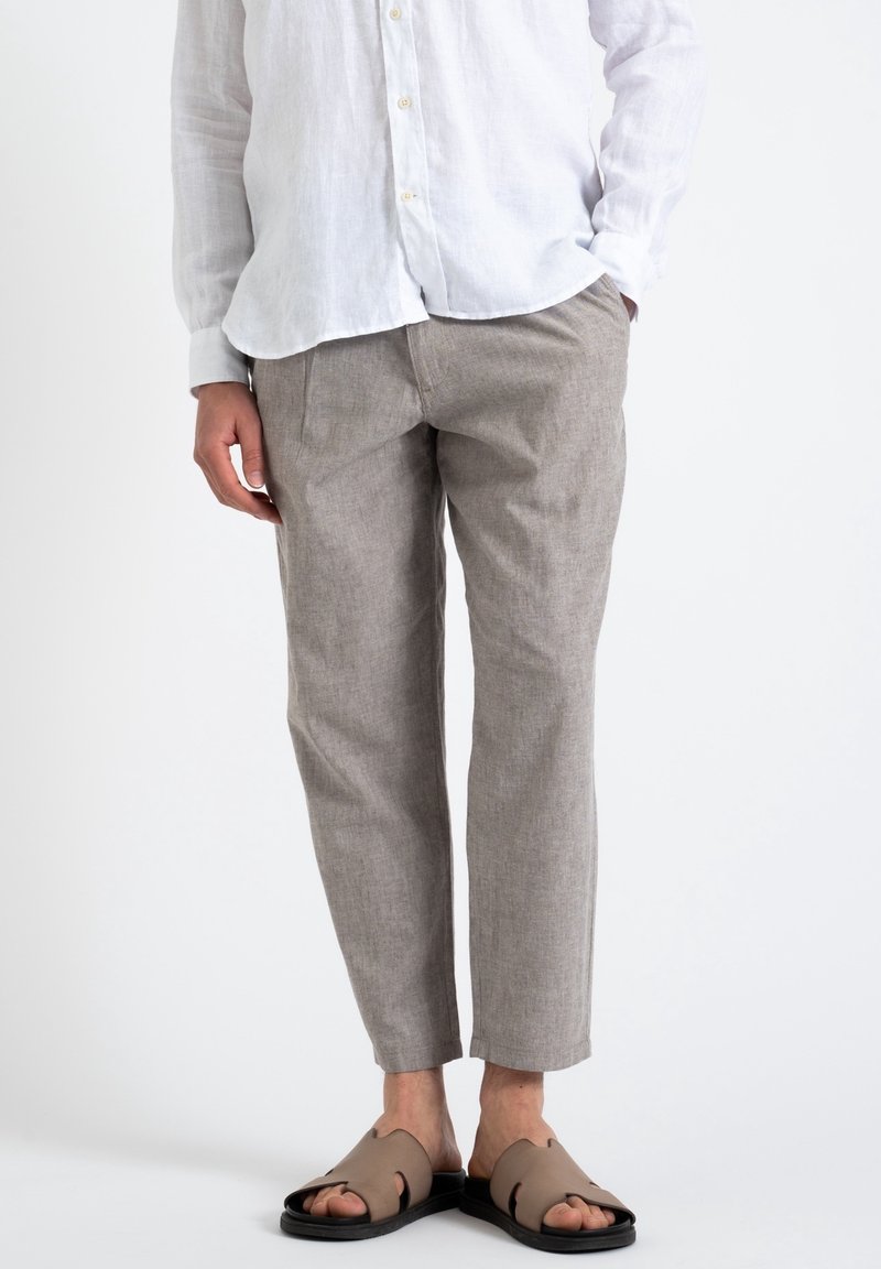 Jasnoszare lniane spodnie o luźnym kroju, z krótkimi nogawkami i subtelną fakturą, zestawione z brązowymi klapkami z wycięciami.