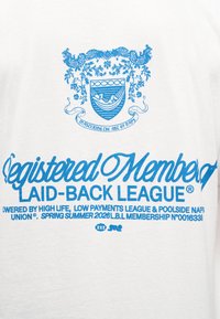 Μπλε έμβλημα με ένα άτομο που χαλαρώνει σε αιώρα, λουλουδένιες λεπτομέρειες και κείμενο "Εγγεγραμμένο Μέλος της Χαλαρής Λίγκας" σε λευκό ύφασμα.