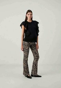 Μαύρη μπλούζα με φουσκωτά μανίκια, συνδυασμένη με μπεζ παντελόνι με τύπωμα ζέβρας. Και τα δύο κομμάτια έχουν εφαρμοστή γραμμή και λεία υφή.