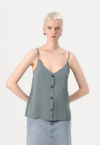 Camiseta de tirantes finos en gris claro, con escote en V y botones en la parte delantera. El material parece suave. Combinada con una falda de mezclilla.
