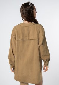 Langärmliges, lässig geschnittenes Hemd aus einem strukturierten beige Stoff. Mit einem Rückenpasse und knöpfbaren Manschetten. Glatte, weiche Oberfläche mit einem entspannten Design.