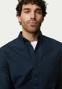 Camisa de algodón azul marino tipo botonadura con cuello, bolsillo en el pecho y puños de doble botón; textura suave con características de diseño mínimas.