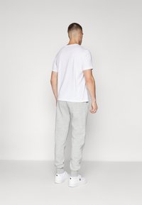 Grijze sweatpants en een wit T-shirt met korte mouwen, voorzien van een klassieke ronde hals, gecombineerd met witte sneakers. Achteraanzicht weergegeven.