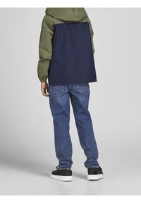 Chaqueta con capucha en verde y azul marino, con puños elásticos, combinada con jeans azules y zapatos negros. La chaqueta presenta un diseño de bloques de color.
