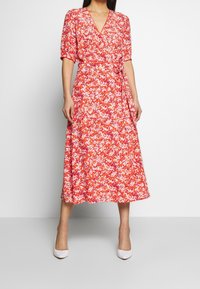 Robe midi à imprimé floral rouge avec un décolleté en V, des manches courtes bouffantes et une taille à nouer, fabriquée en tissu léger, présentant une silhouette fluide.