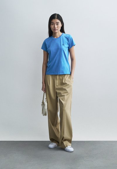 Kék pamut rövid ujjú póló, laza bézs nadrággal párosítva. A fehér tornacipő és egy kis krémszínű kézitáska teszi teljessé a szettet.