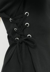 Το μαύρο τοπ διαθέτει πλευρικό κορδόνι με ασημένιες τρύπες και λεπτομέρεια δεσίματος. Μαλακό, ελαστικό ύφασμα με ομαλή υφή.