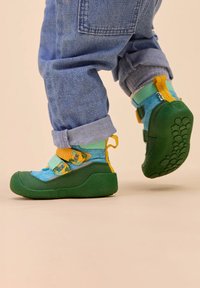 Scarpe per bambini verdi e blu con suola in gomma testurizzata, dotate di cinturini gialli, collo imbottito e dettagli a stampa giocosi.