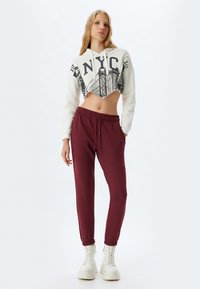Hvid cropped hoodie med trykt NYC-design, parret med bordeaux joggers med elastiske manchetter. Modellen har hvide platformstøvler på.