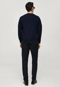 Marinblå tröja med rund halsringning, ribbat avslut och texturerad tyg. Matchas med mörka byxor och svarta skor. Modellen sedd bakifrån.