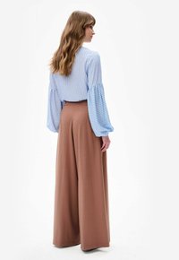 Jasnoniebieska bluzka w białe paski z bufkowymi rękawami, zestawiona z brązowymi spodniami o szerokich nogawkach i wysokim stanem. Gładkie tkaniny, luźny krój.