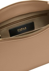 Interno di borsa in pelle beige che mostra una cerniera dorata e un'etichetta nera con la scritta "Furla Since 1927" impressa in lettere dorate.