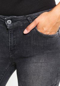 Vaqueros de denim negros con una textura suave, que cuentan con un bolsillo frontal, cierre de botón y un ligero desgastado en la tela.