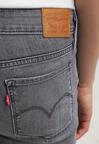 Jeans de denim gris con un parche de cuero de Levi Strauss & Co., diseño de bolsillo trasero con costura oculta y acento con etiqueta roja.