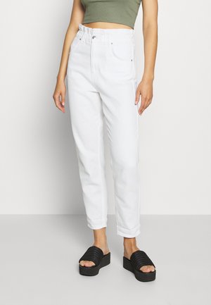 Witte hoge taille jeans met een ontspannen pasvorm, voorzien van een geplooide tailleband, zijzakken en opgerolde hemden, gecombineerd met zwarte platform sandalen.