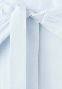 Gros plan d’un col de chemise blanc avec un gros nœud de tissu à l’avant, montrant une texture de tissu lisse et nette.