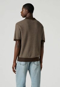 Ruskea neulepolo, jossa on houndstooth-kuosi, lyhyet hihat ja ribbaushiresut. Yhdistetty vaaleansinisiin väljät farkkuihin.