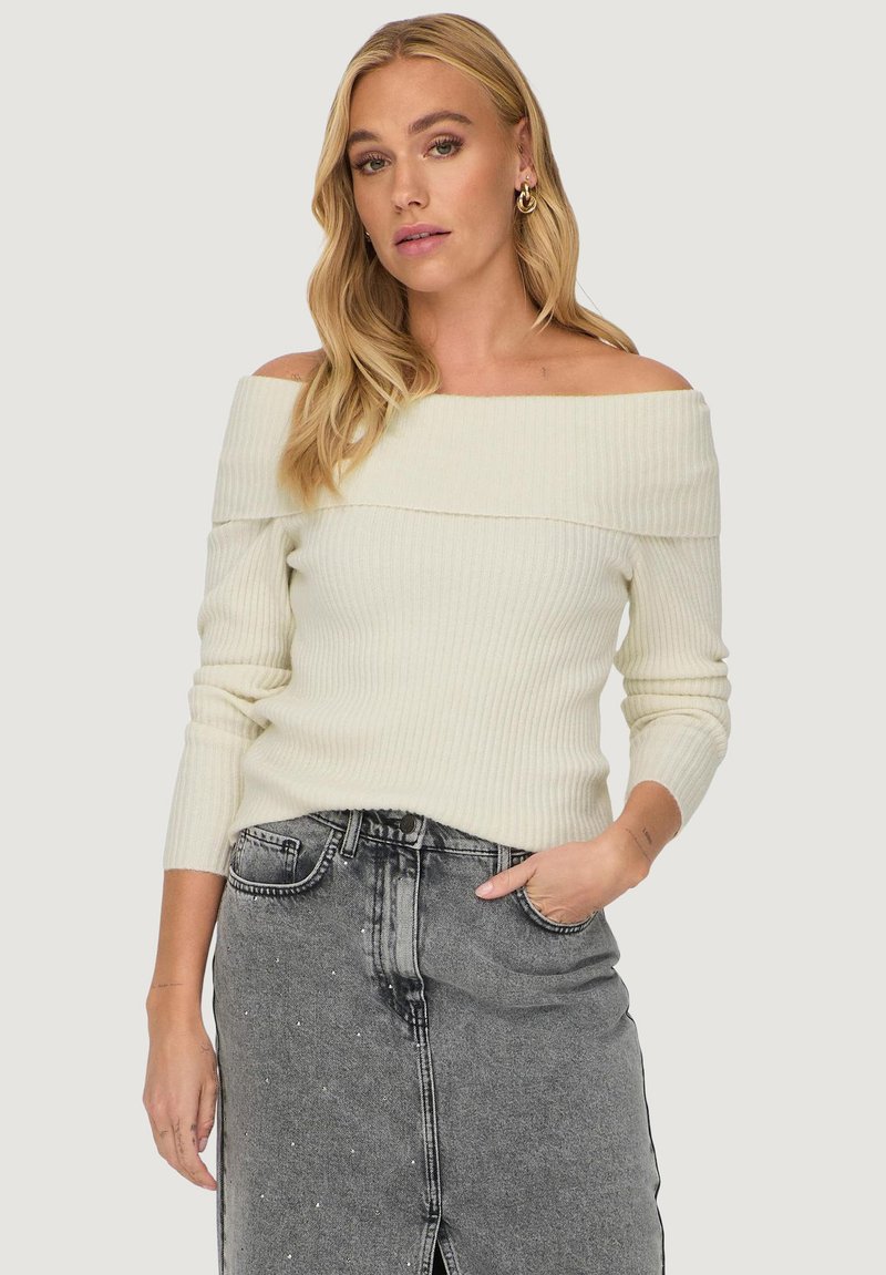 Off-white off-the-shoulder ribbed sweater with long sleeves, paired with a gray denim skirt featuring a front slit and embellishments.