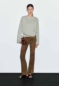 Grijze lange mouwen top, bruine suède wijde broek, gouden riem, bruine clutch en zwarte sandalen; gladde texturen en neutrale kleuren.