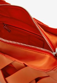 Red shoulder bag with a glossy finish, featuring a zip closure, lined interior, and a woven exterior detail. Inner tag visible.