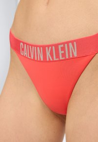 Κόκκινο εσώρουχο Calvin Klein με φαρδιά ελαστική ζώνη που φοριέται στον κάτω κορμό και τους γοφούς ενός ατόμου.