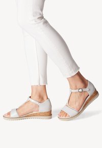 Sandales gris clair avec un talon en liège, bout ouvert, design en T, détails texturés et sangle de cheville réglable.